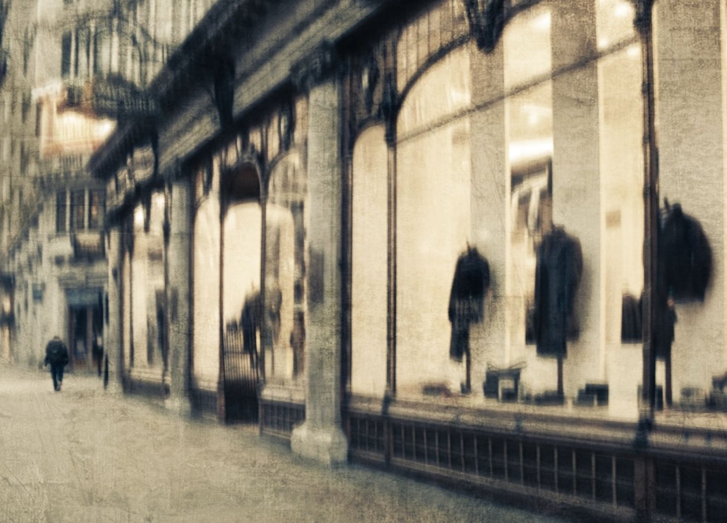 Softly blurred London street scene with a pedestrian walking past illuminated shop windows displaying coats and reflections