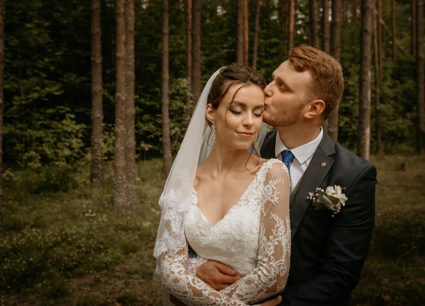 a bride and groom kissing in a forest