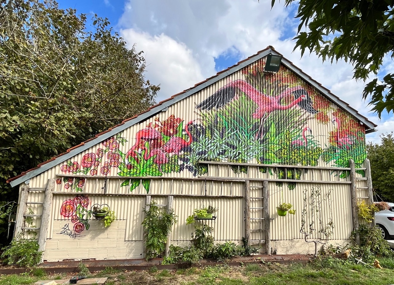 une grange en taule et une fresque avec des flamands roses et des plantes