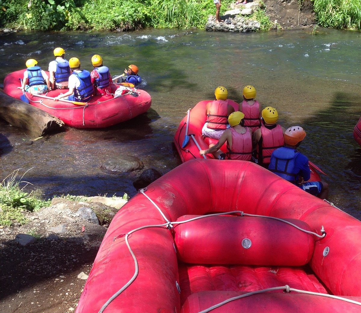 Adventure seekers wearing helmets and life jackets prepare for white water rafting in red inflatable boats on a river.