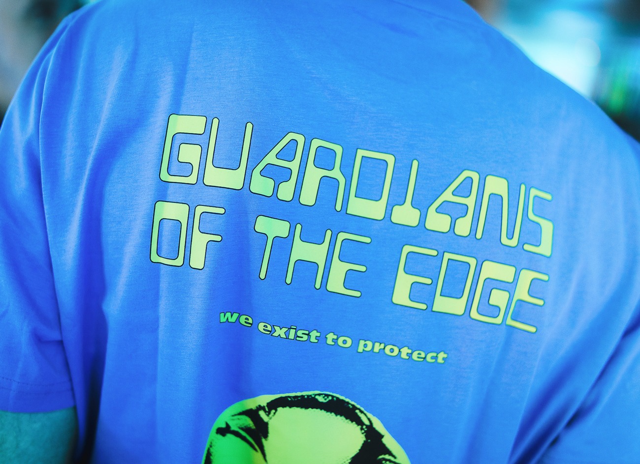 Back of a blue t-shirt with Guardians of the Edge text in a lime green graphic font.