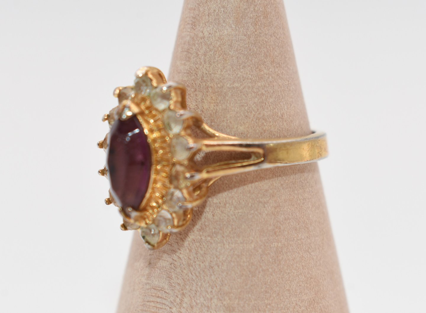 Vintage gold tone ring featuring a large oval red ruby color w/rhinestone halo setting.