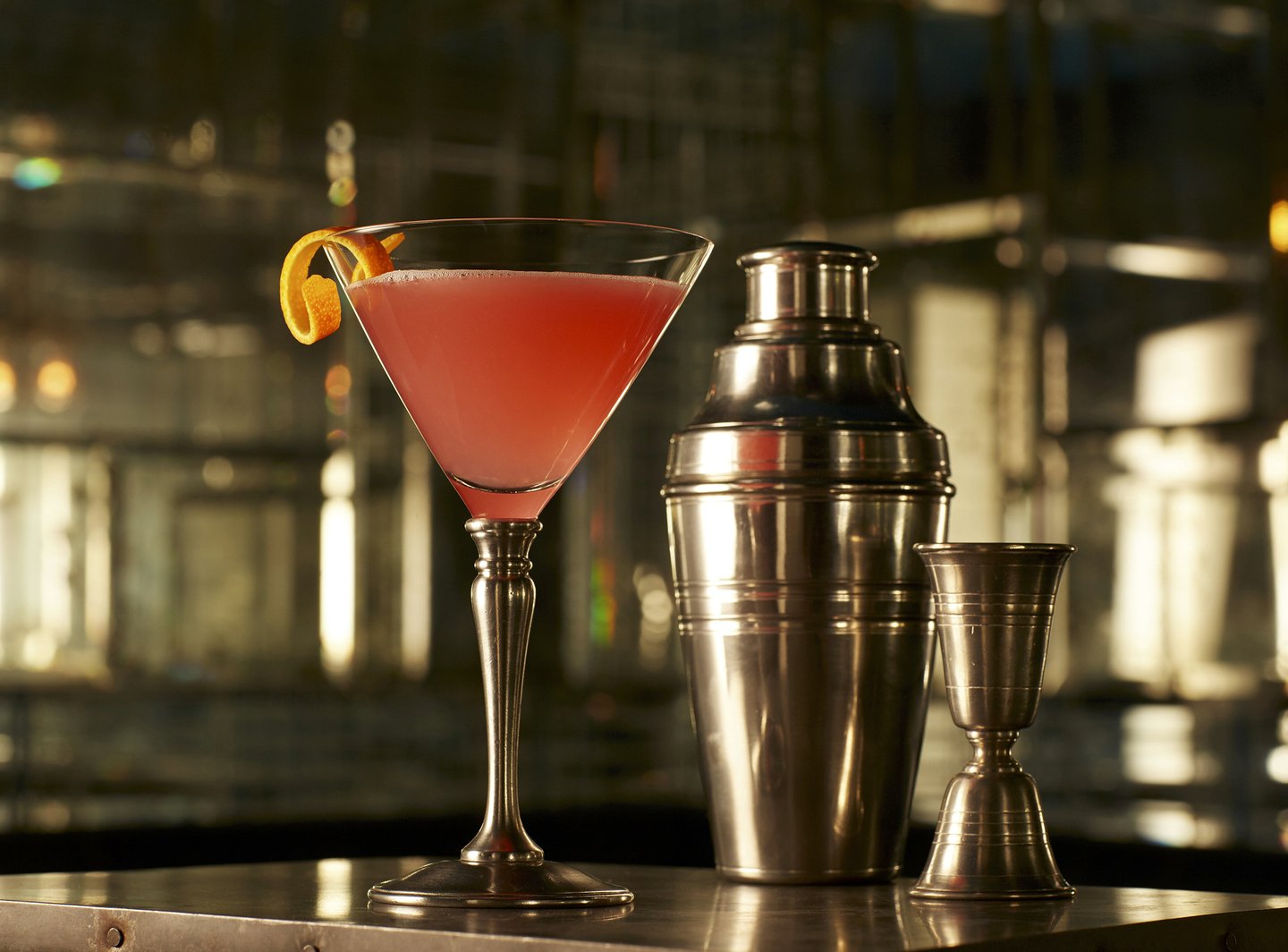Pink cocktail in a glass next to cocktail shaker and measure on a table in Art Deco mirrored bar