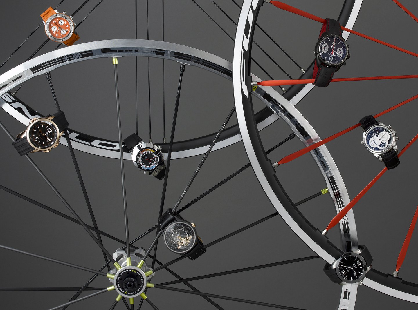 selection of mens watches attached to the spokes of bicycle wheels on a grey background