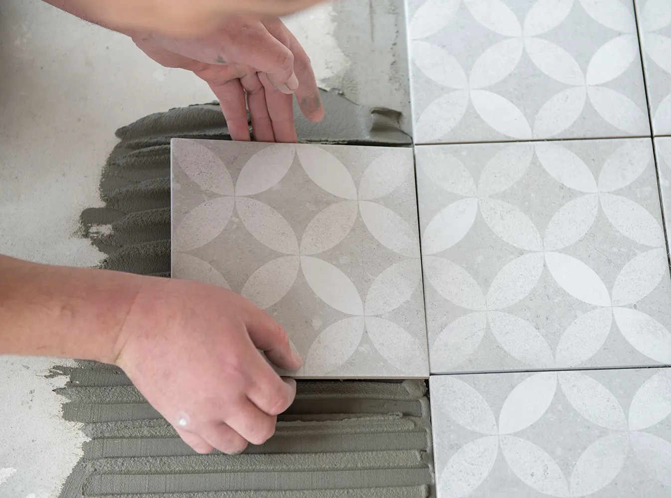 Zbliżenie na płytki, które układa pracownik. Płytki są układane bez fug