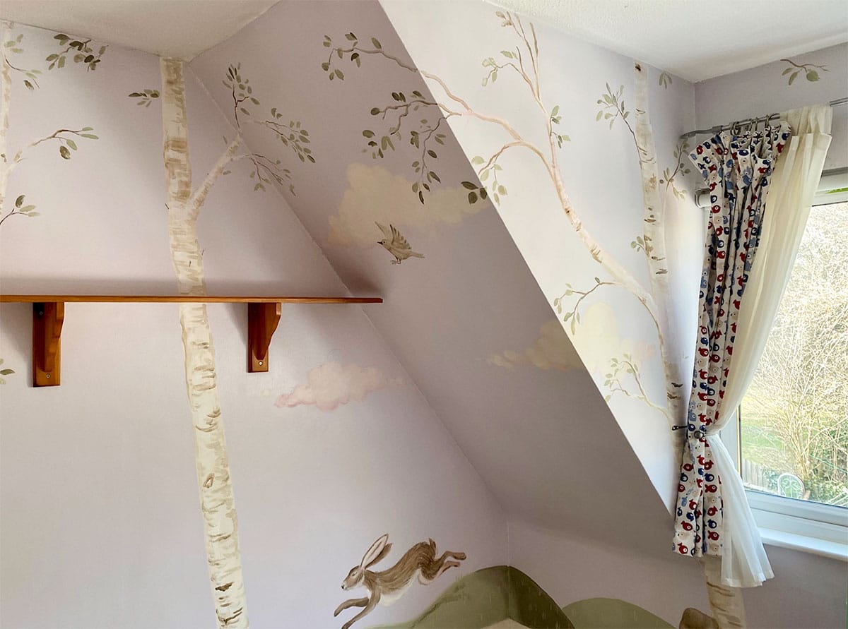 Wide angle on a wrap-around kid’s mural with a painted birch grove and a hare jumping on green ground.