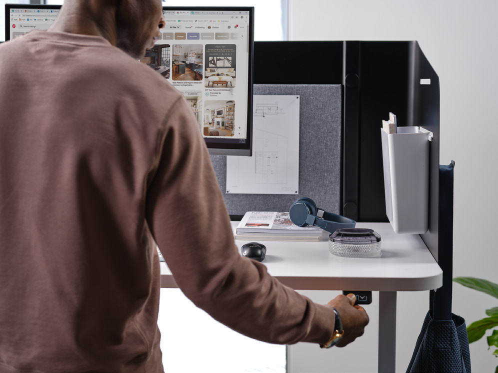 a man in a brown sweater is standing in front of a computer monitor
