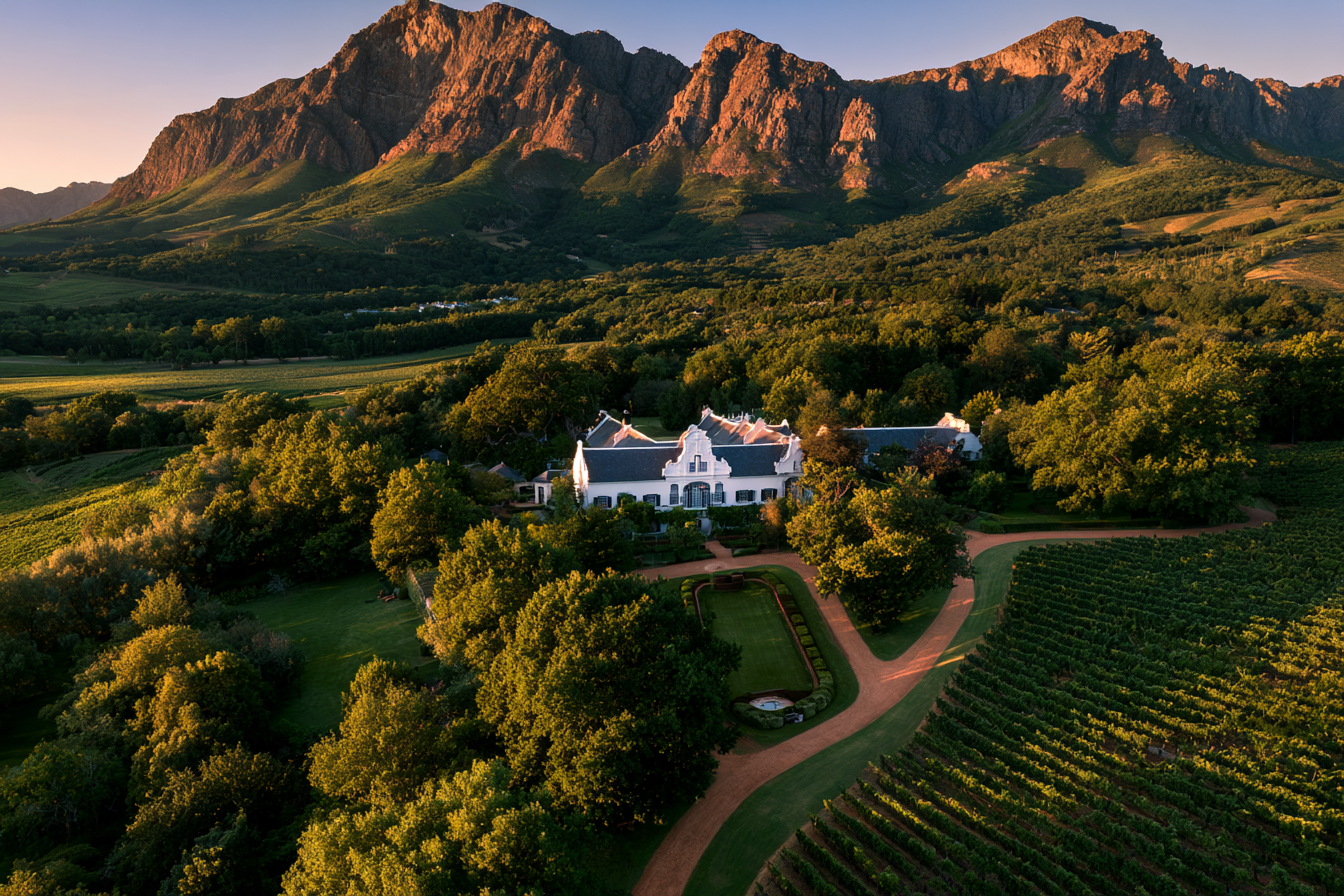 Aerial view of a Cape Dutch manor house and vineyard estate at sunset in Stellenbosch, South Africa.