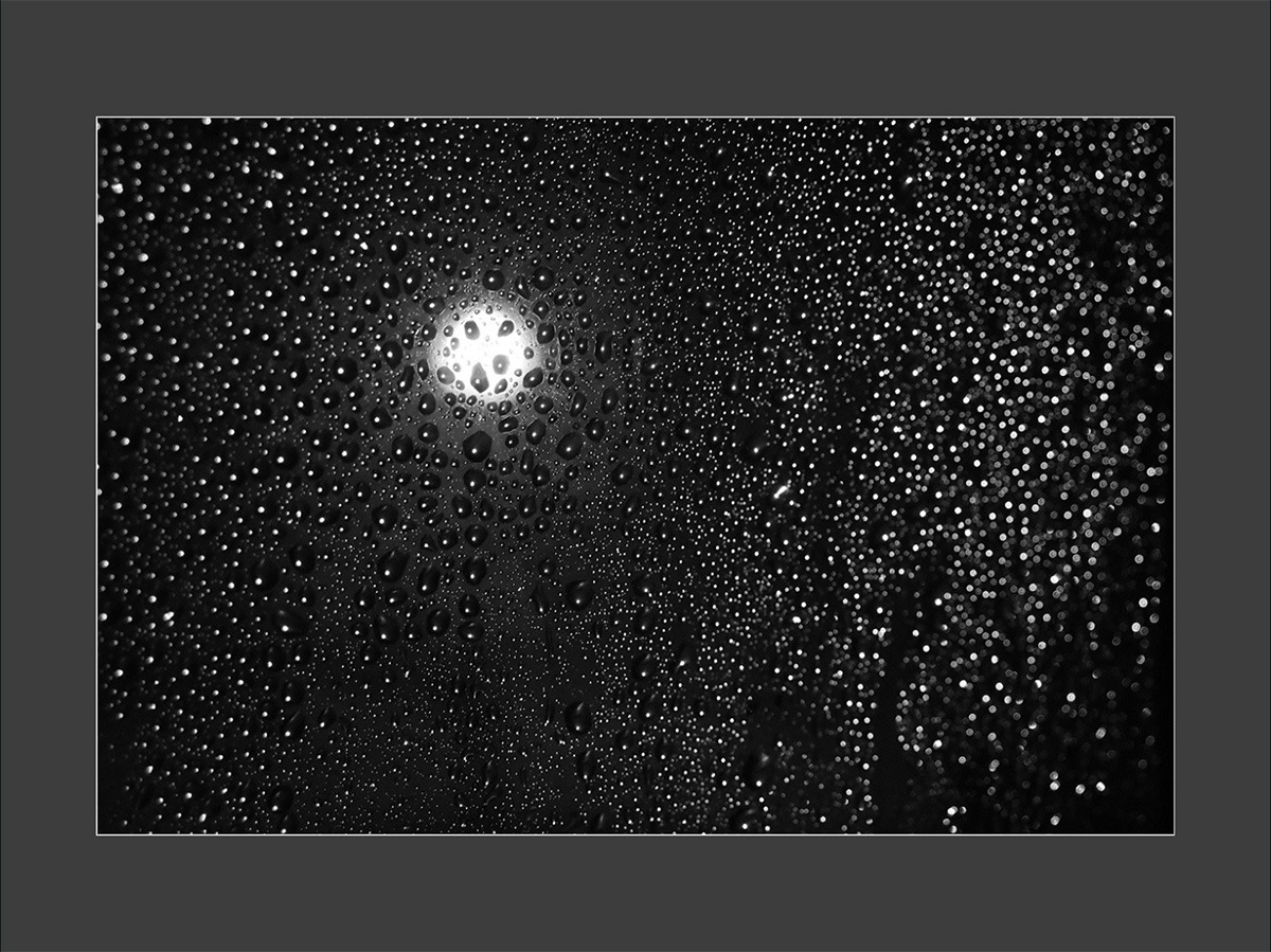 a black and white photo of a lamp post through a rainy window
