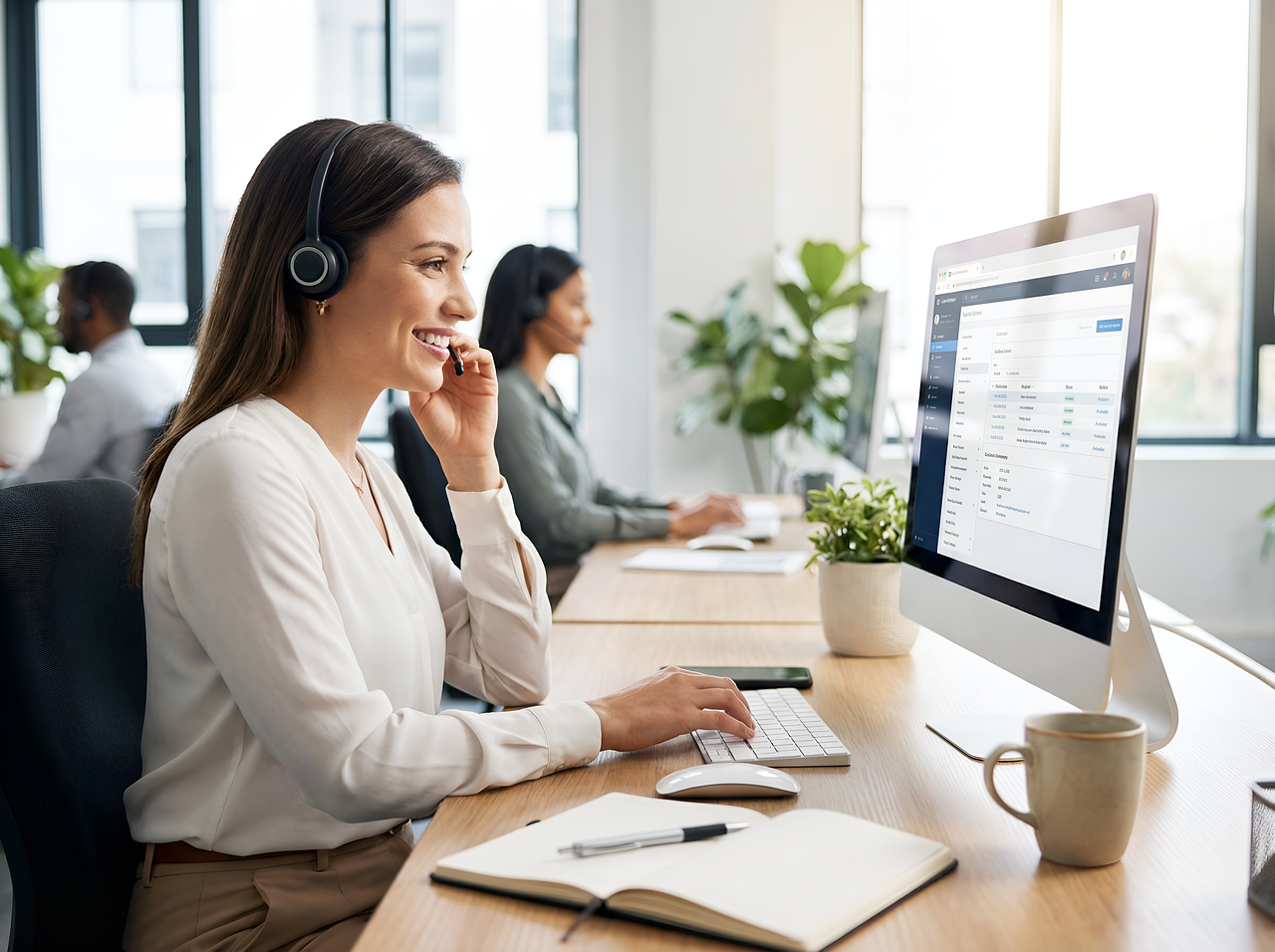 Smiling customer service representative with headset working on a computer in a modern office.