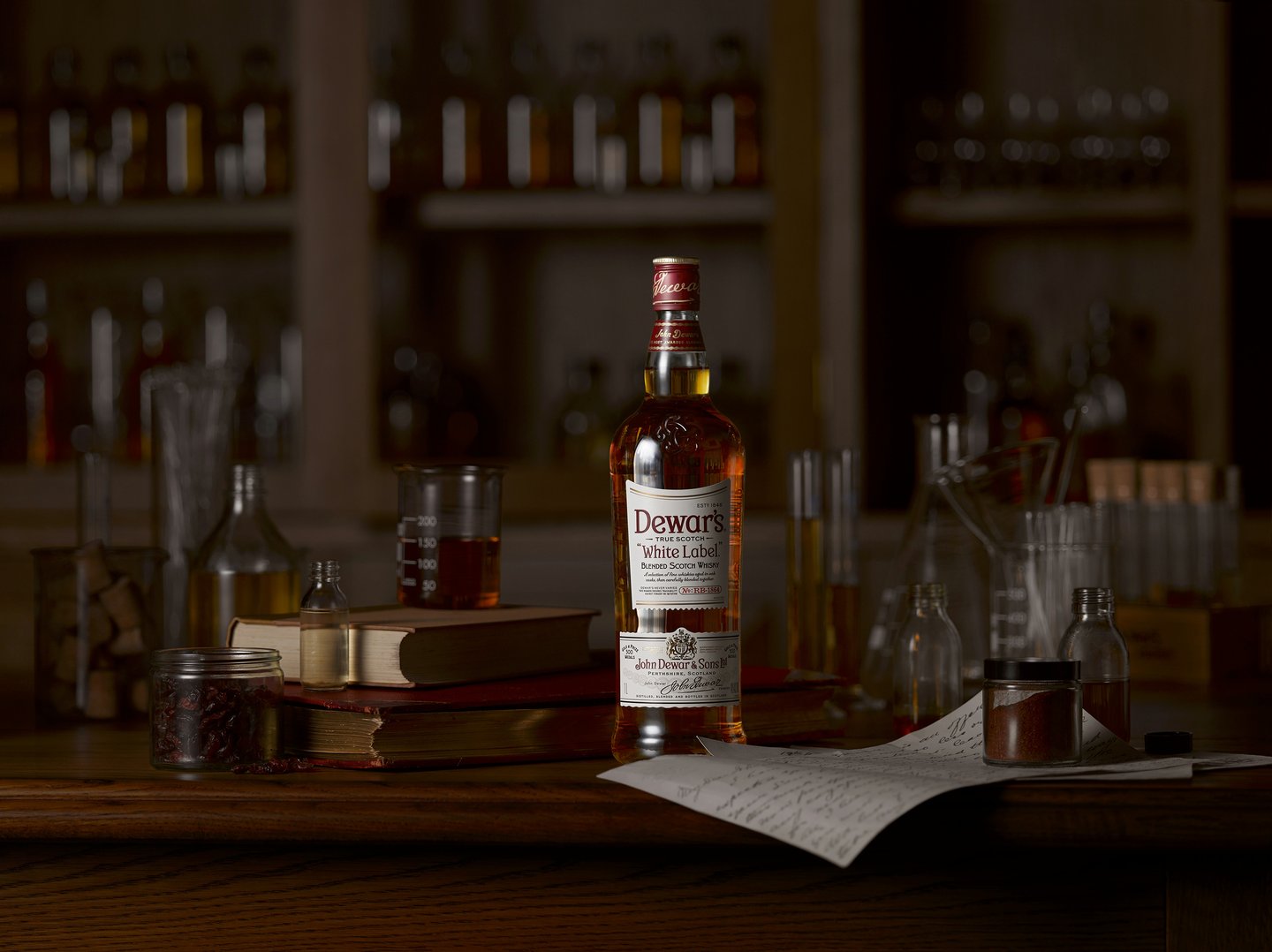 Dewars whisky bottle on a wooden table surrounded by books and glass beakers