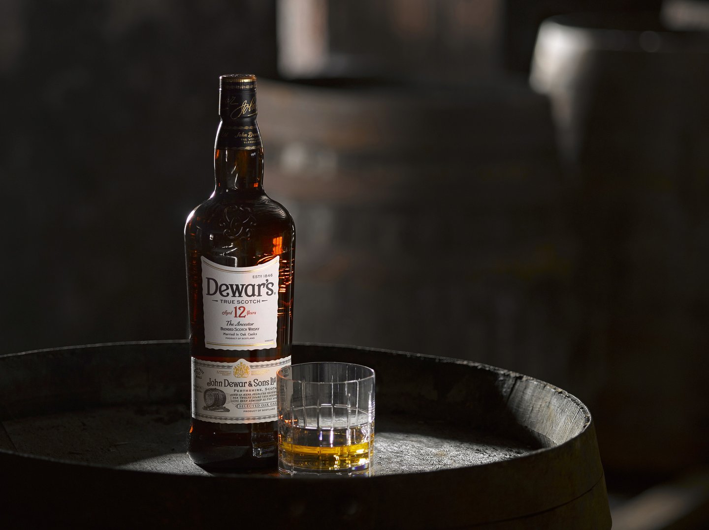 Dewars whisky bottle and glass on a wooden barrel