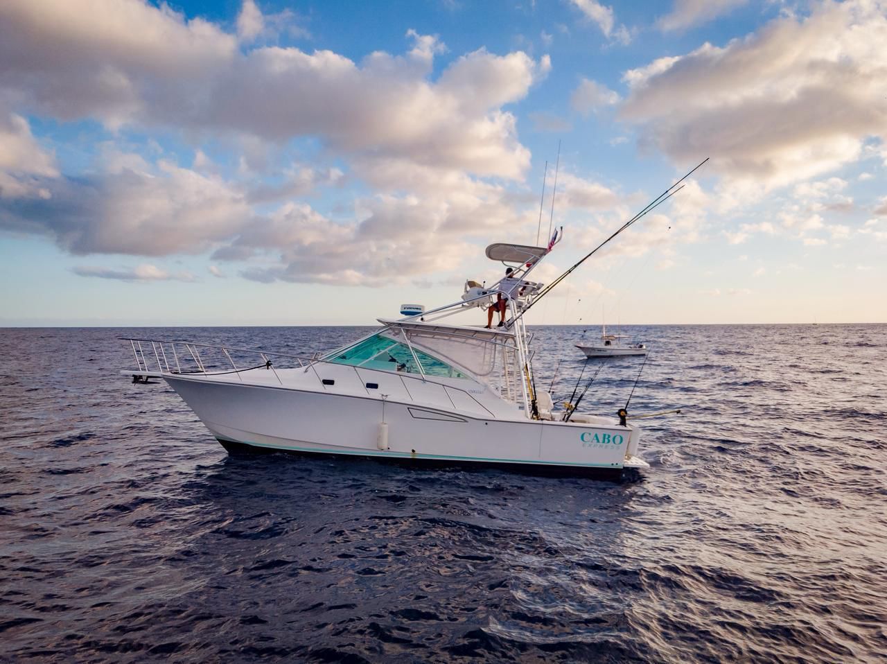 A white Cabo Express sportfishing boat with fishing rods on the open ocean under a cloudy sky.