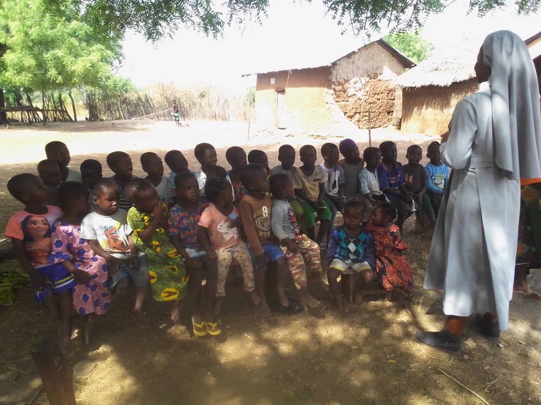 Missionary sister teaching children outdoors in Ghana community