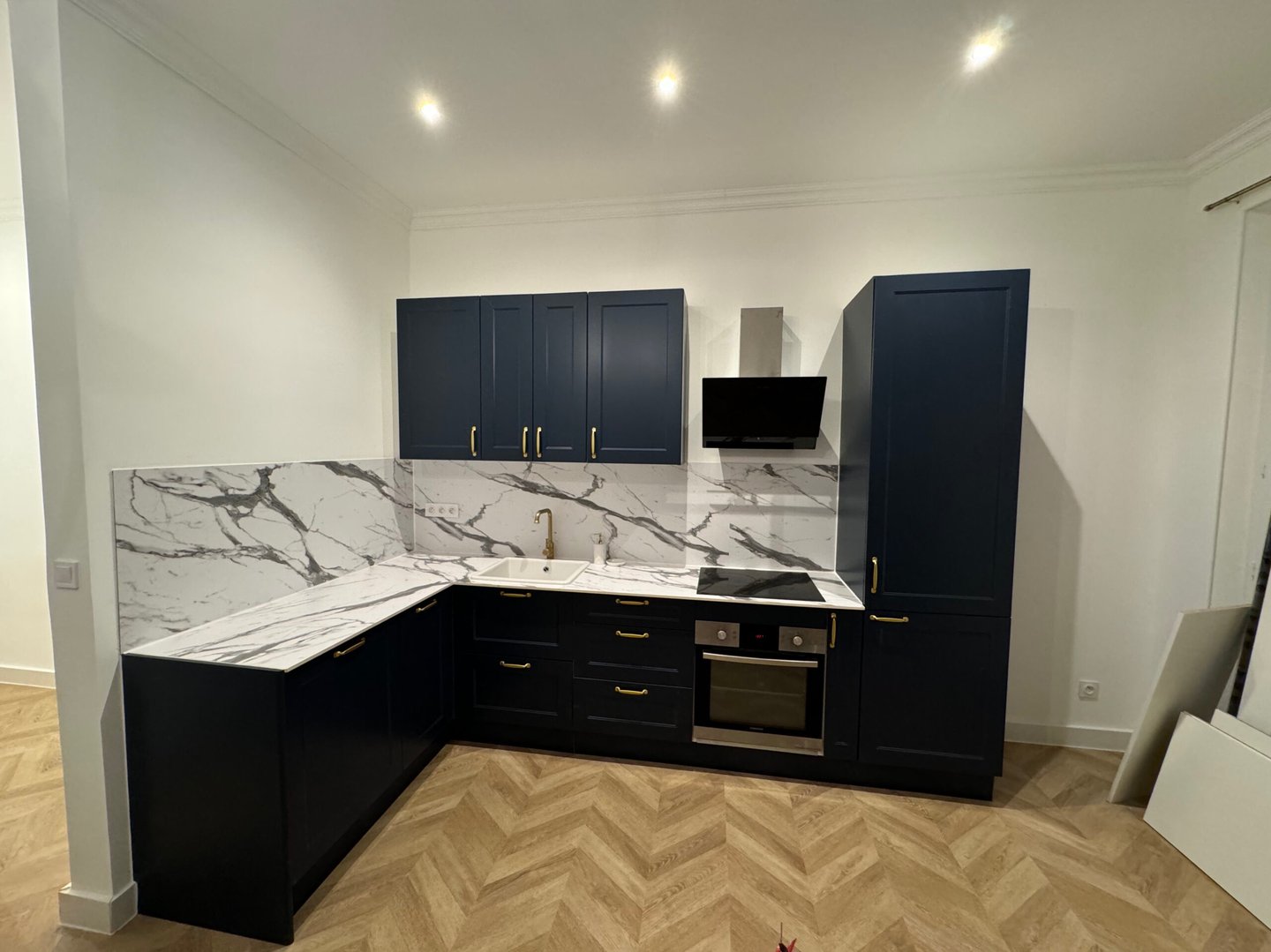 Réalisation d'une cuisine équipée avec plan de travail en marbre, meubles noirs et parquet chevron. Harenova