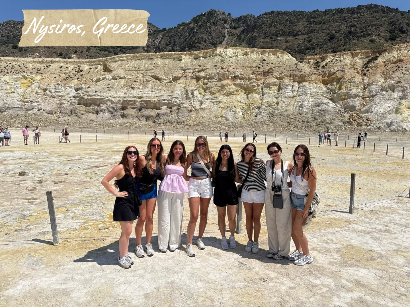 A group of women travelers posing inside the volcanic crater of Nisyros, Greece, with rocky terrain behind.