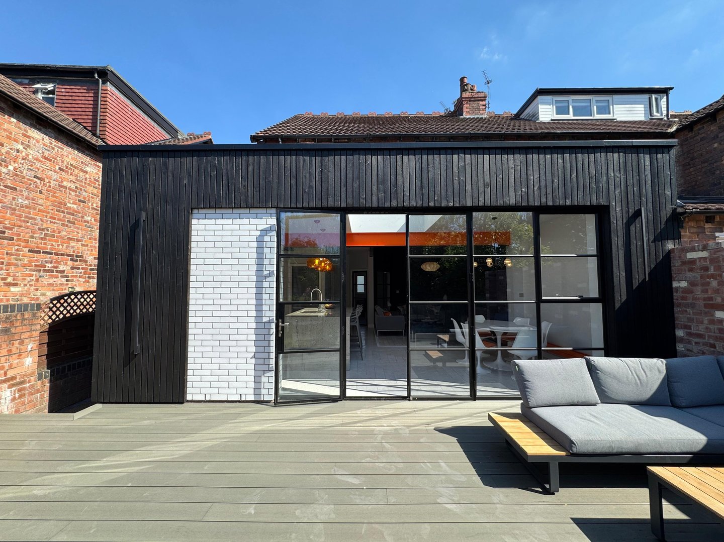 Modern home extension featuring black timber cladding and large glass Crittall doors opening onto a wooden deck.