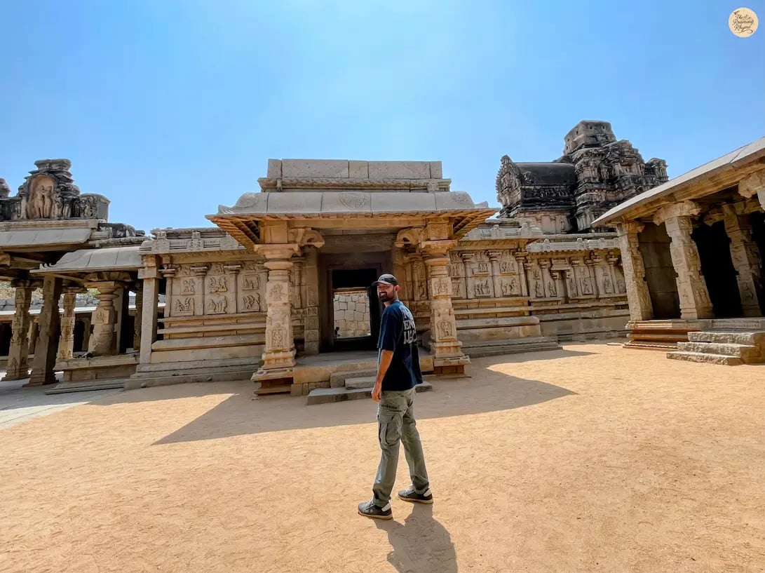 Person standing at Hazara Rama Temple in Hampi, with walls depicting Ramayana carvings.