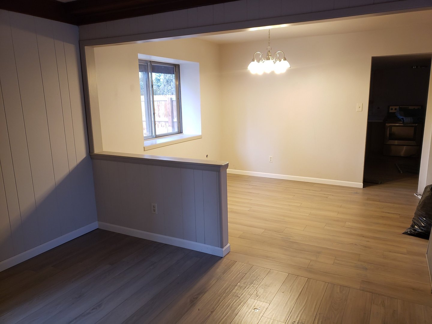 Newly renovated empty dining room with light oak laminate flooring and neutral grey paneled walls.