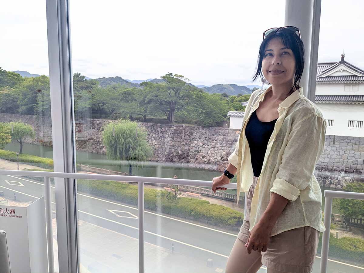 Woman standing beside a large window overlooking Sunpu Castle and its moat in Shizuoka.