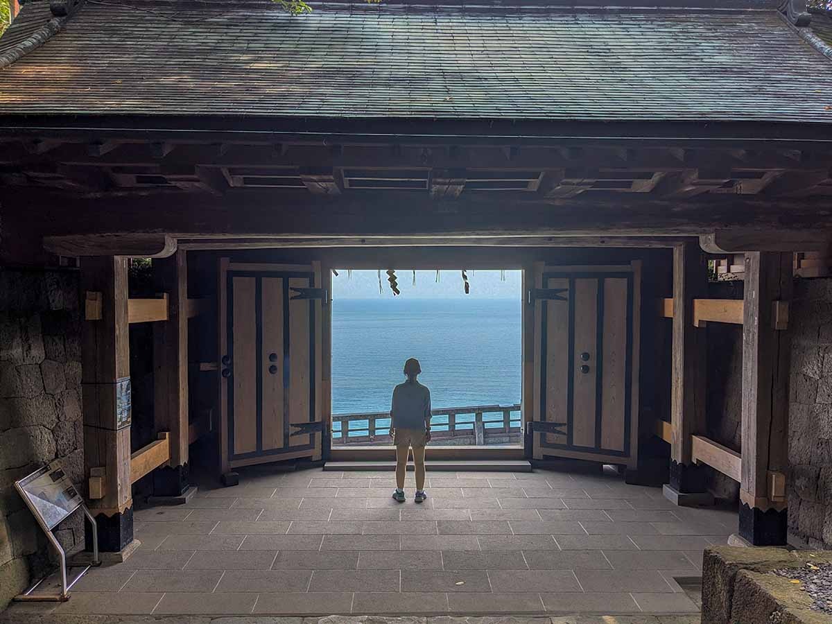 Silhouette of a woman framed by a temple gate with ocean views beyond in Shizuoka, Japan.