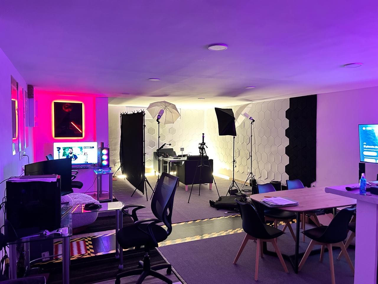 Professional podcast and video production studio with purple LED lighting, softboxes, and acoustic wall panels.