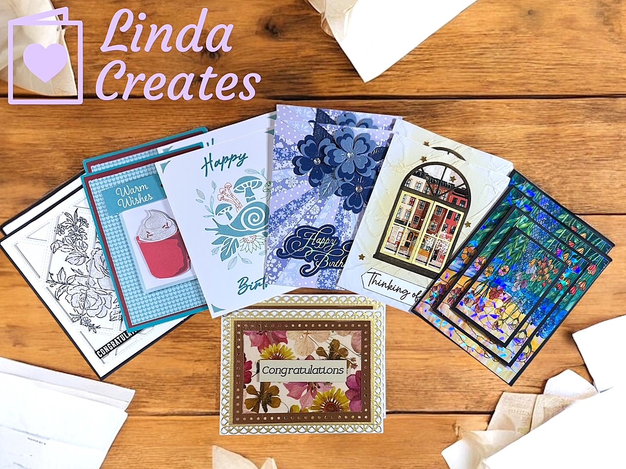 An array of handmade cards laying on a wooden desk.
