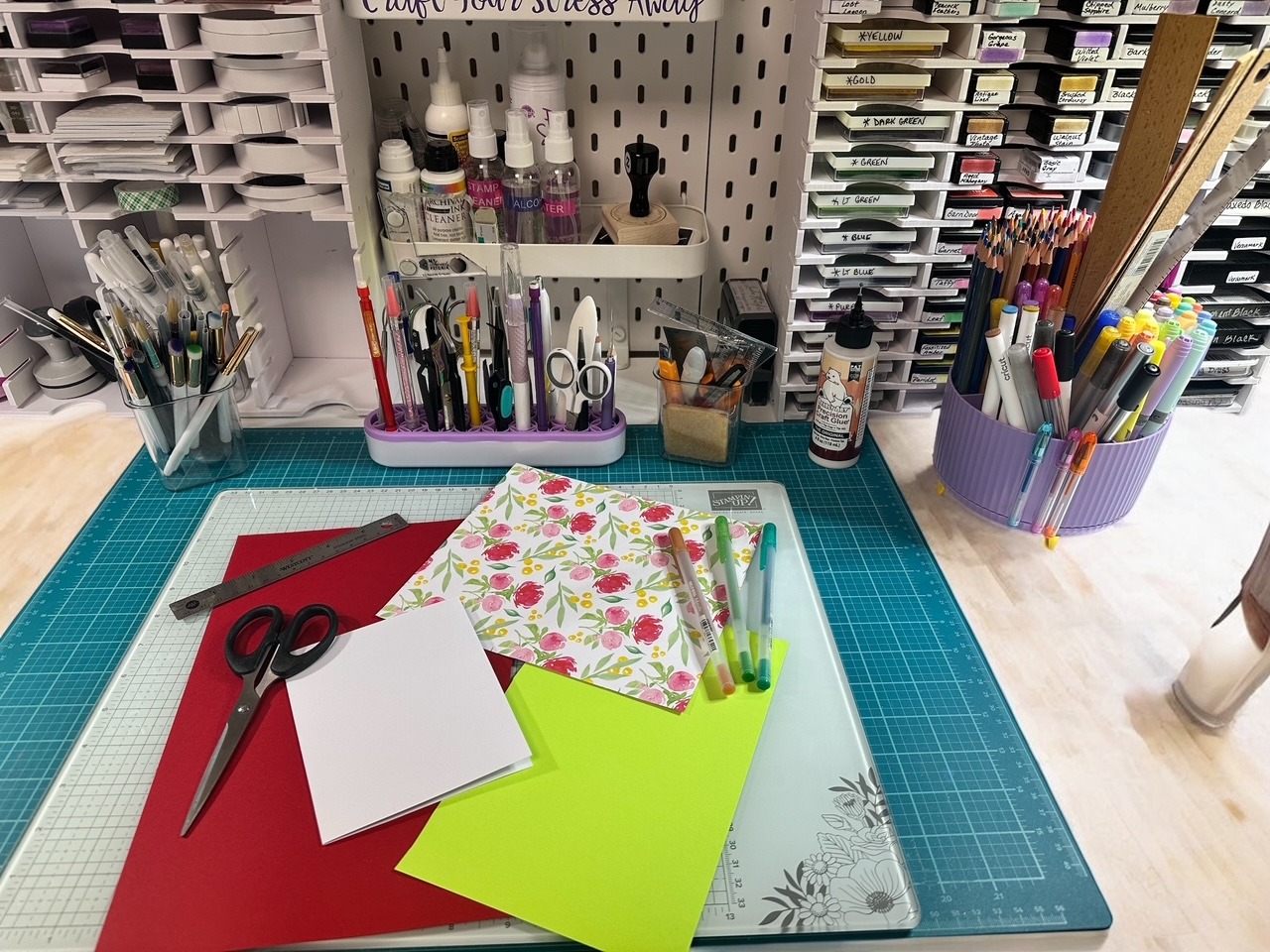 Desk with a variety of craft tools, paper, scissors, ruler and various writing tools. 