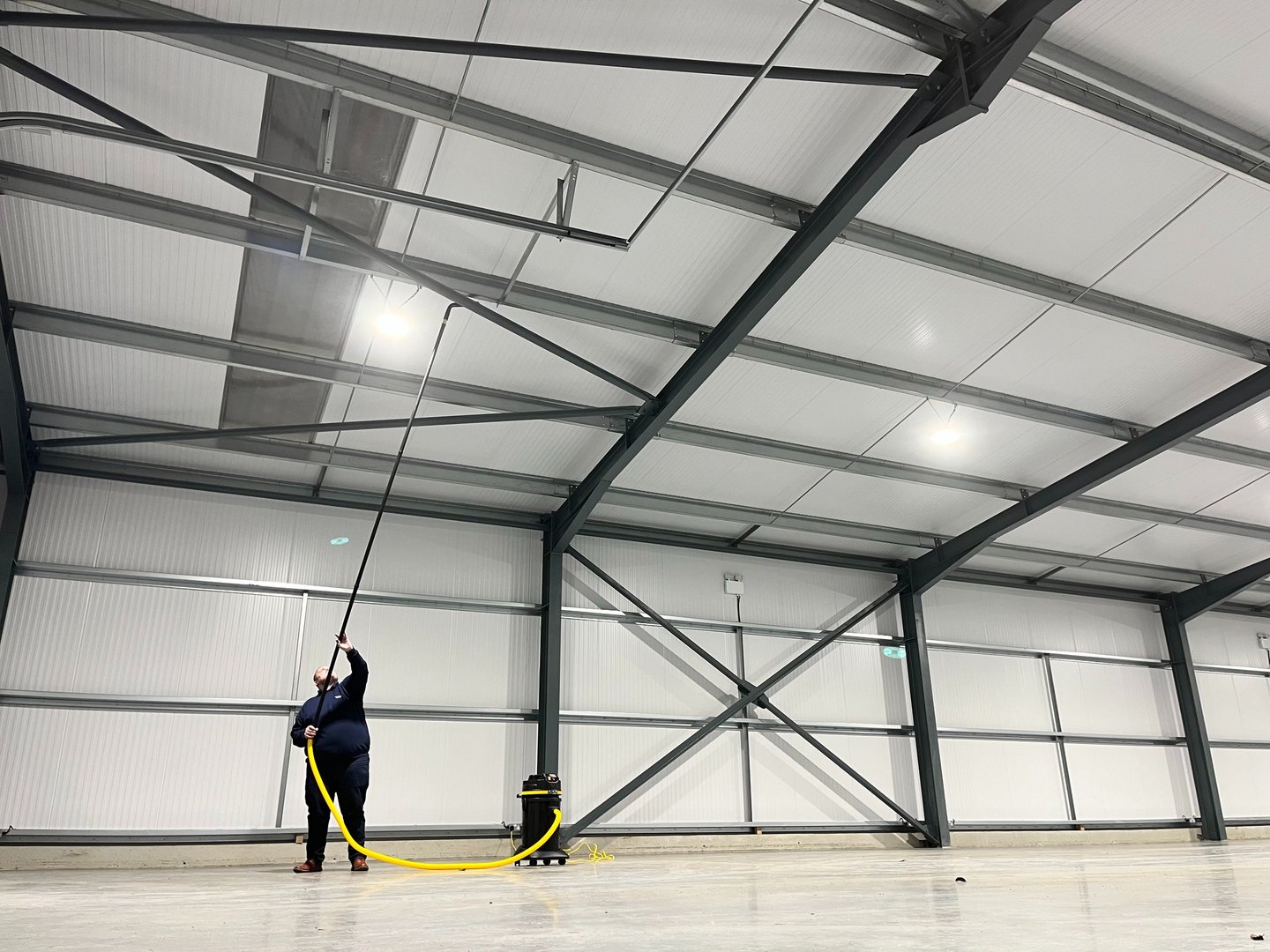 Technician vacuuming high level ceiling from the ground