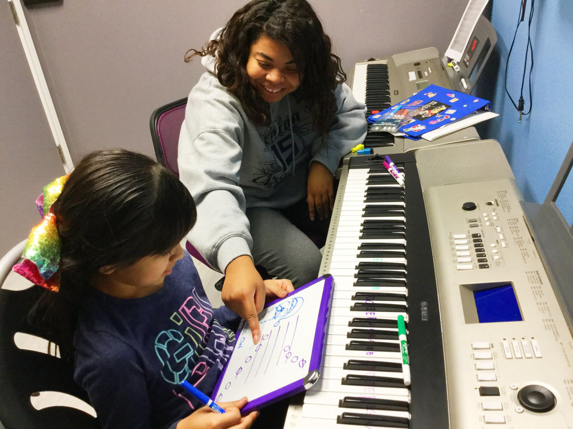a smiling woman sitting at a piano with a young girl