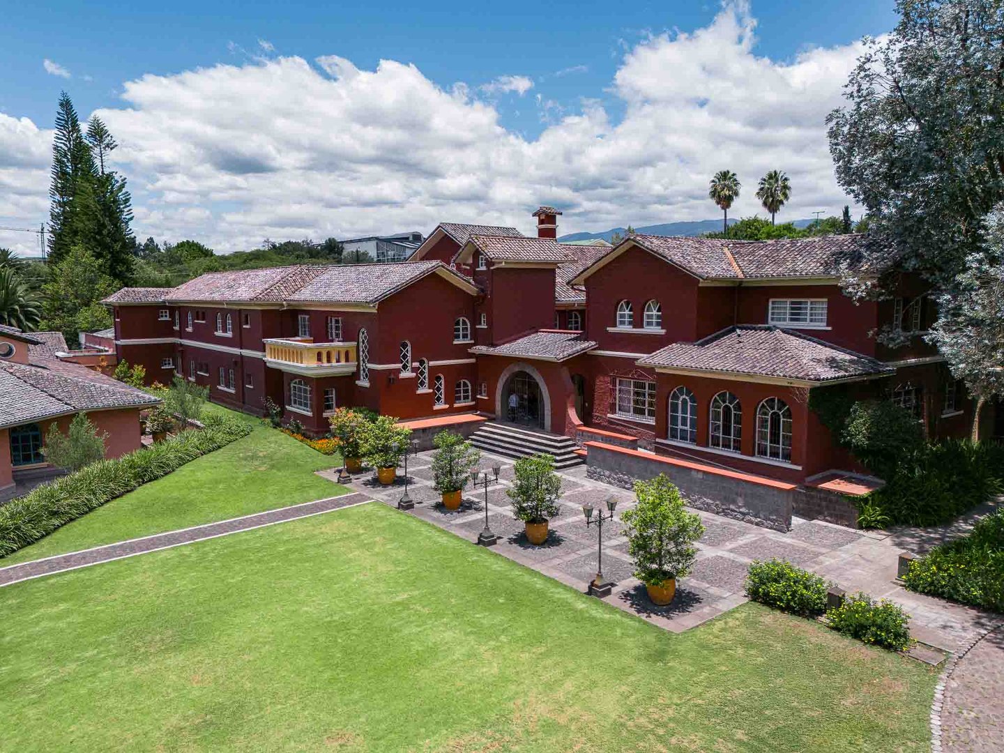 Fotografía aérea de gran casa religiosa de color rojo rodeada de hermoso  jardín verde en Quito Ecuador