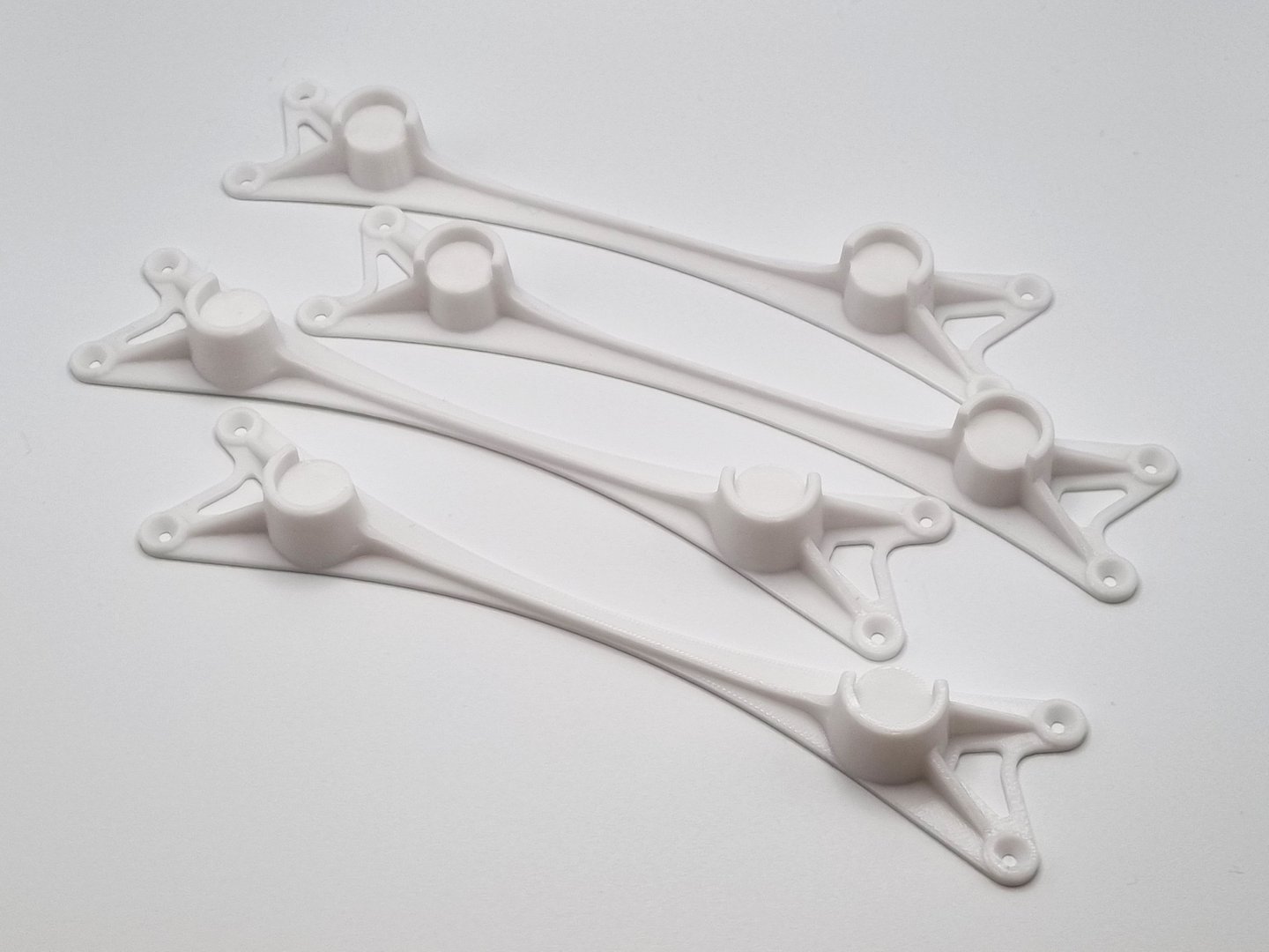 Four white plastic 3D printed drone frame arm replacements arranged on a white surface.