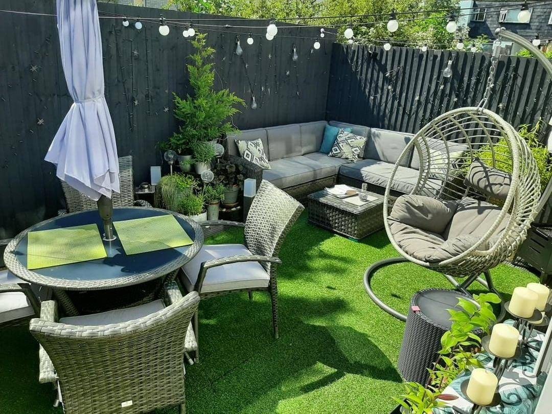Modern patio with rattan garden furniture, artificial grass, a grey corner sofa, and a hanging egg chair.