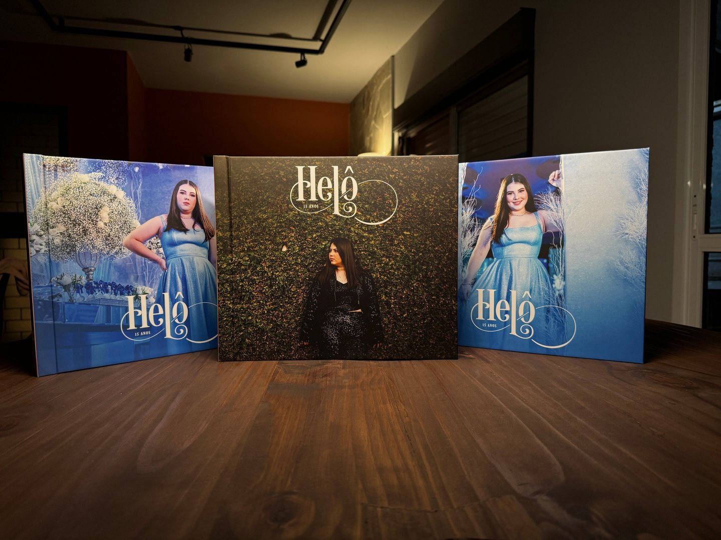 Três álbuns fotográficos de 15 anos com capas personalizadas expostos sobre mesa de madeira.