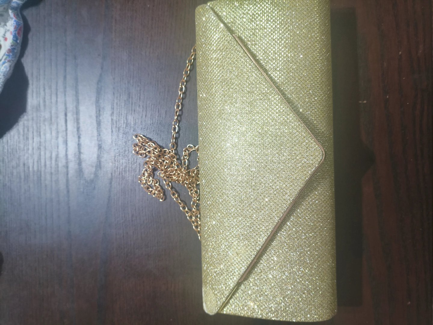 Análise de design de mala clutch dourada estilo envelope com brilho glitter e alça de corrente.