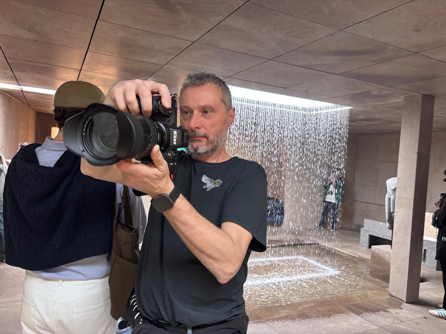 Professional photographer using a Nikon mirrorless camera to capture an indoor waterfall installation.
