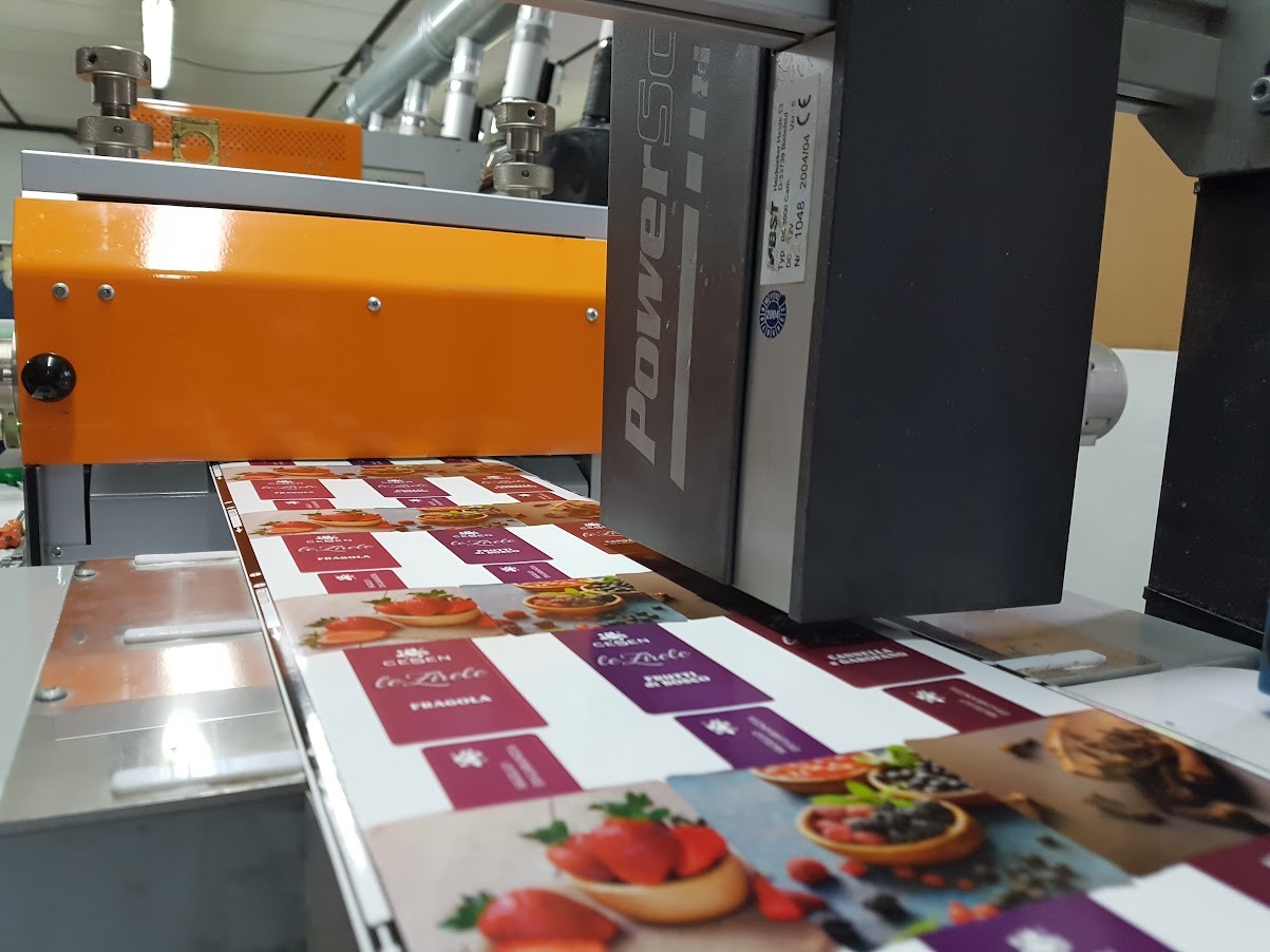 Industrial food packaging machine printing colorful fruit labels on a fast-moving conveyor belt.