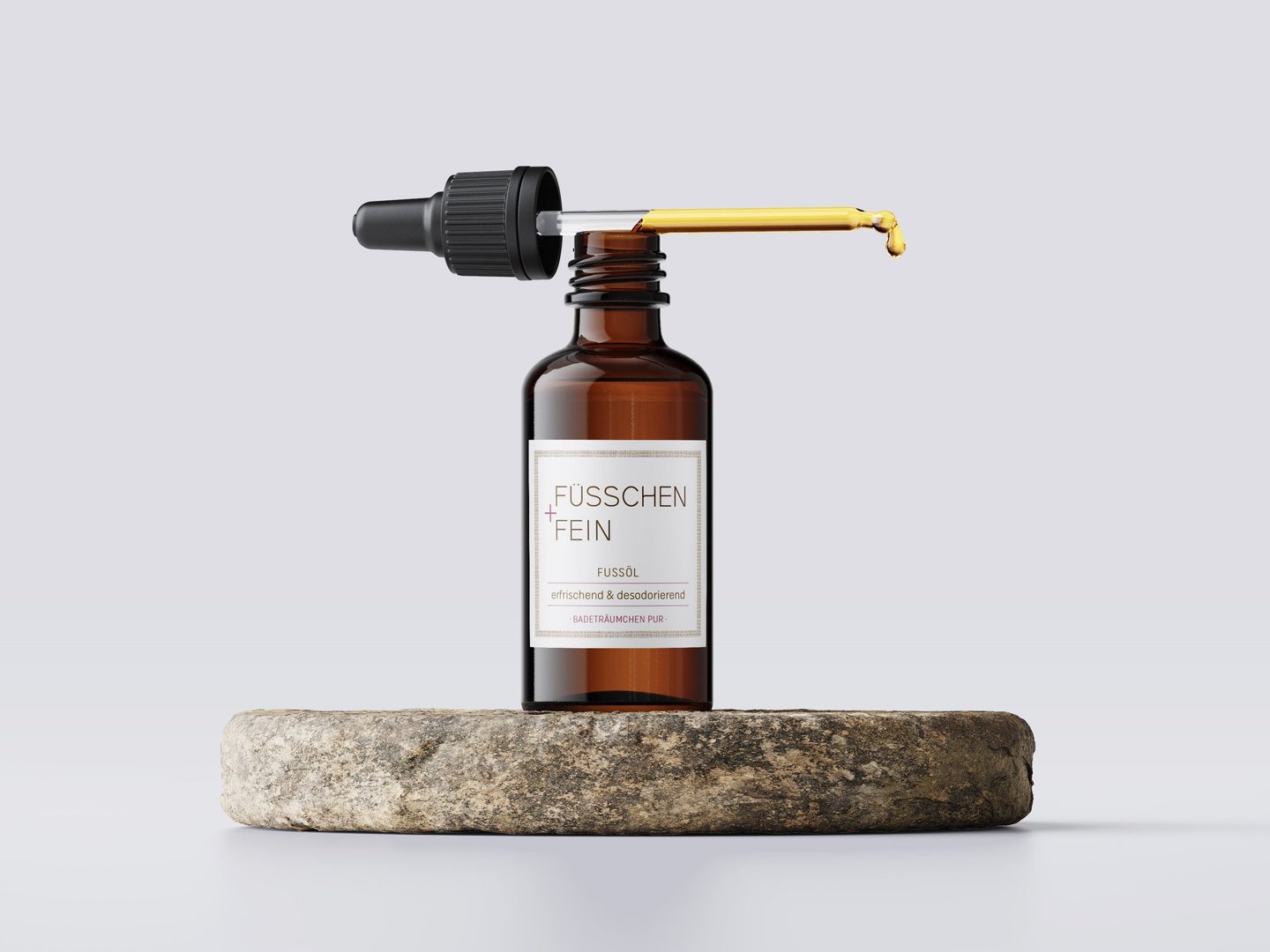 Amber glass dropper bottle with Fußöl essential oil for foot care on a natural stone base.