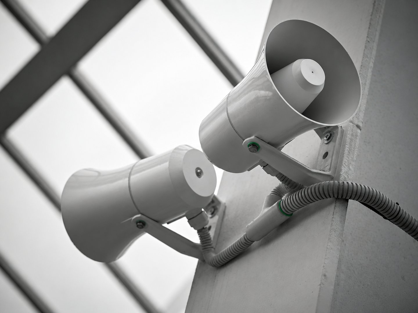 Two white public address system horn speakers mounted on a wall for announcements and audio broadcasting.