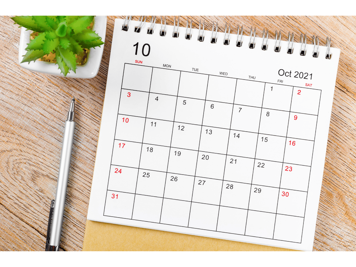 October 2021 monthly desk calendar on a wooden surface with a pen and small green plant.