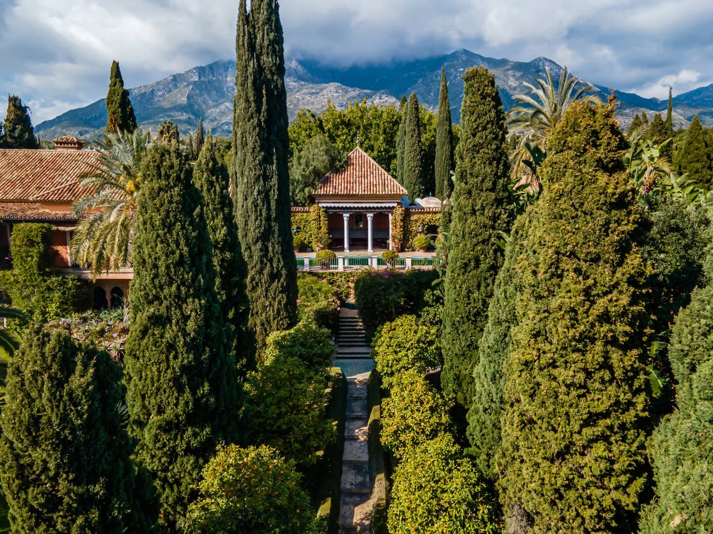 Cypress-lined pathway leading to pool pavilion with mountain backdrop