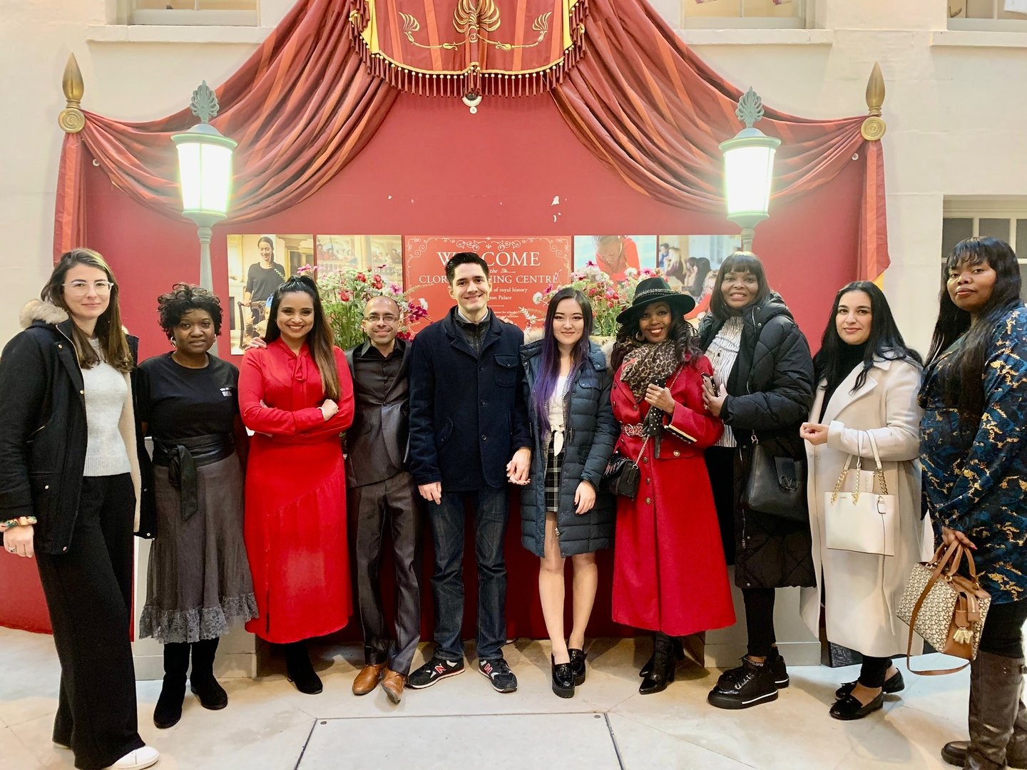 A diverse group of people standing together in front of a red theatrical backdrop and lanterns.