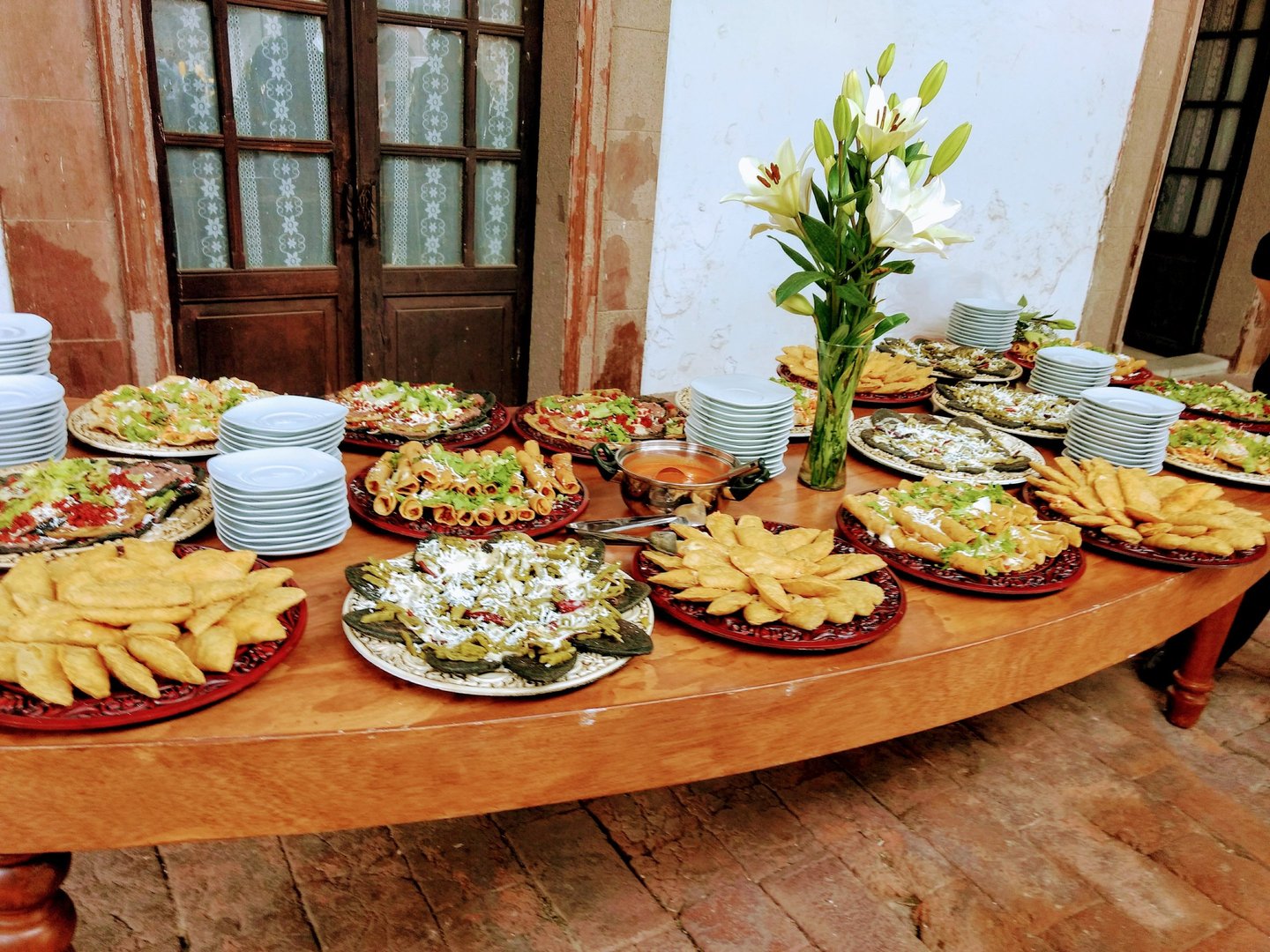 Buffet table with traditional Mexican appetizers, fresh lilies, and stacks of white plates.