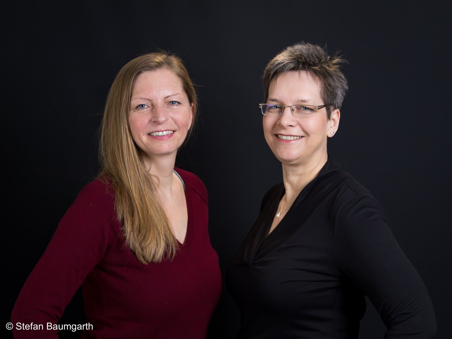 two women standing next to each other in front of a black background