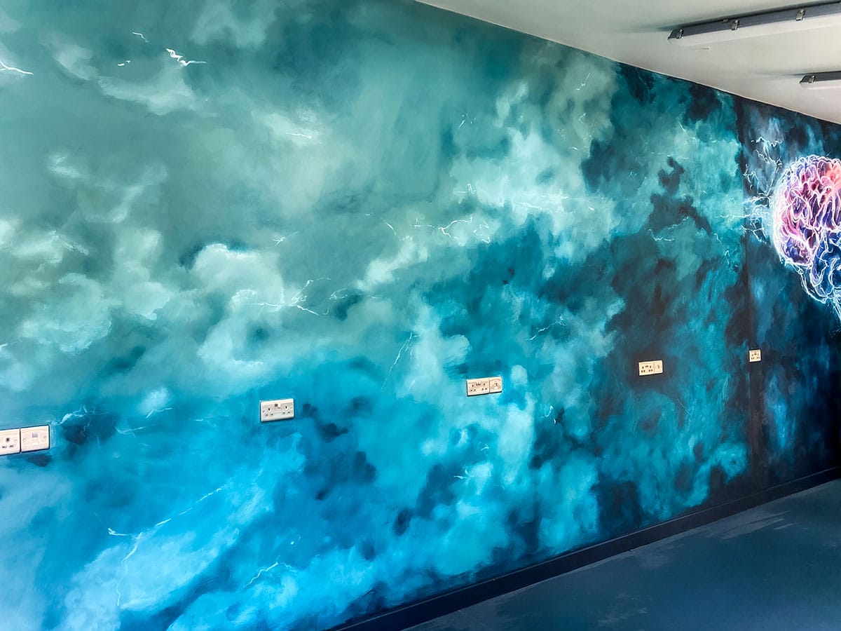 Angled view on mural with teal stormy clouds and a bit of stylised brain in pink and teal colours. 