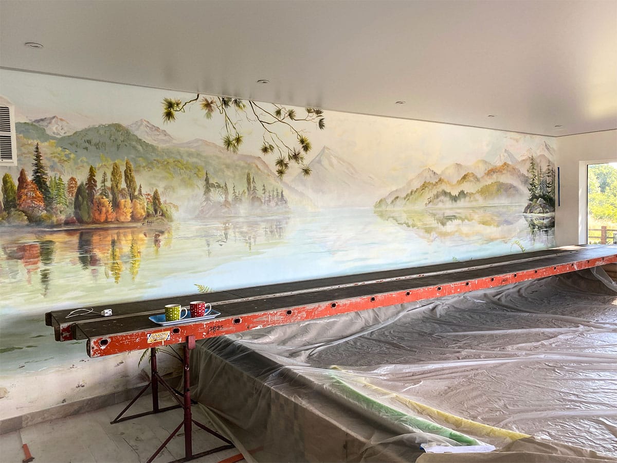 Painted panorama lake mural in progress with scaffold, showing New Zealand mountains and water view.