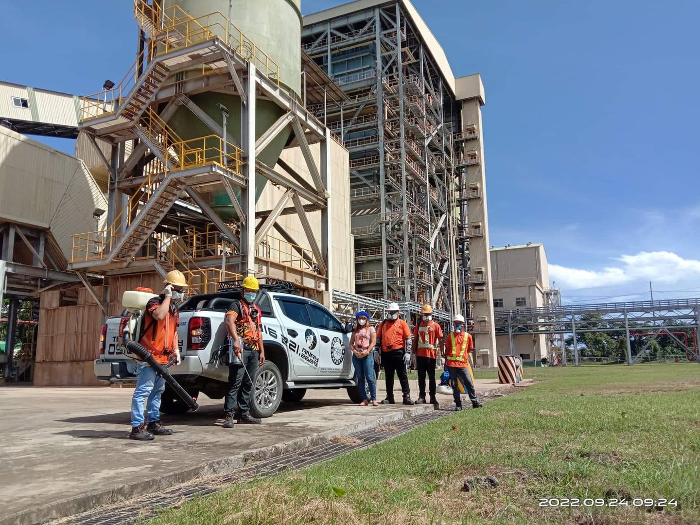 Industrial workers in safety gear standing by a pickup truck outside a power plant facility.