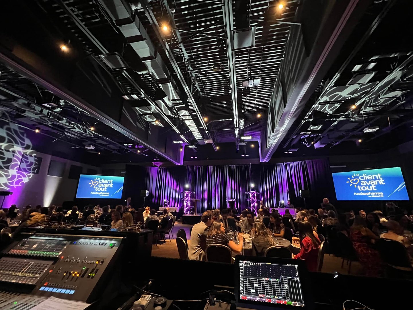 Corporate event gala with guests seated at tables facing a purple stage with AV mixing consoles in the foreground.