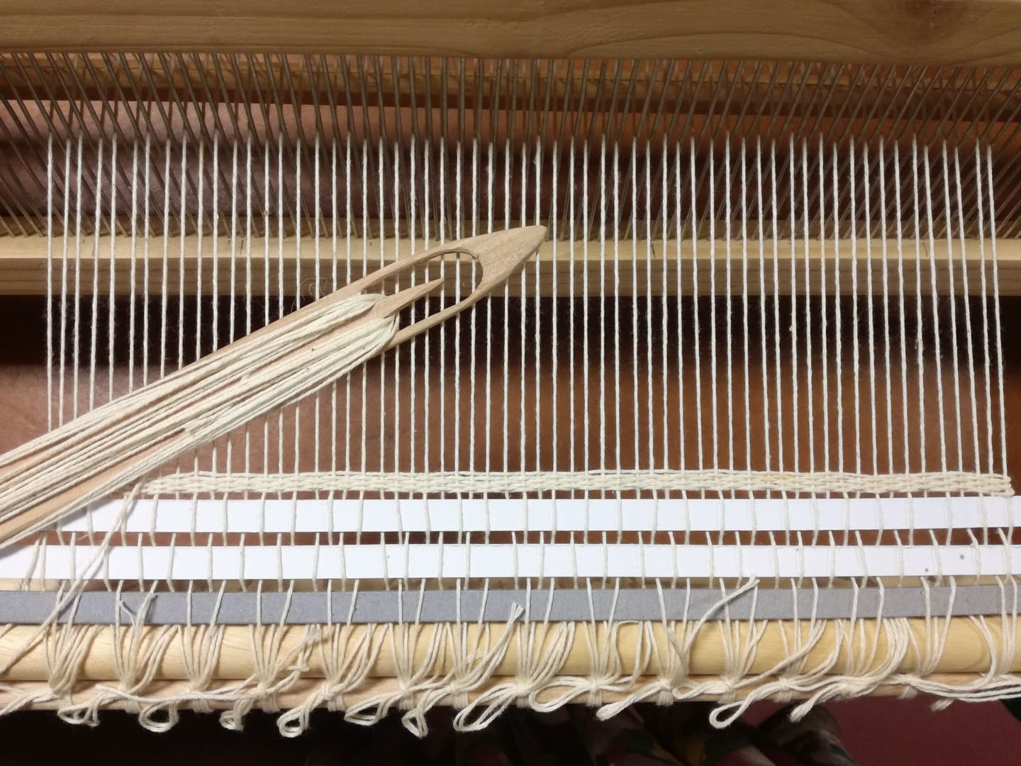 a weaving loom with a white cotton warp and a wooden shuttle with white cotton thread