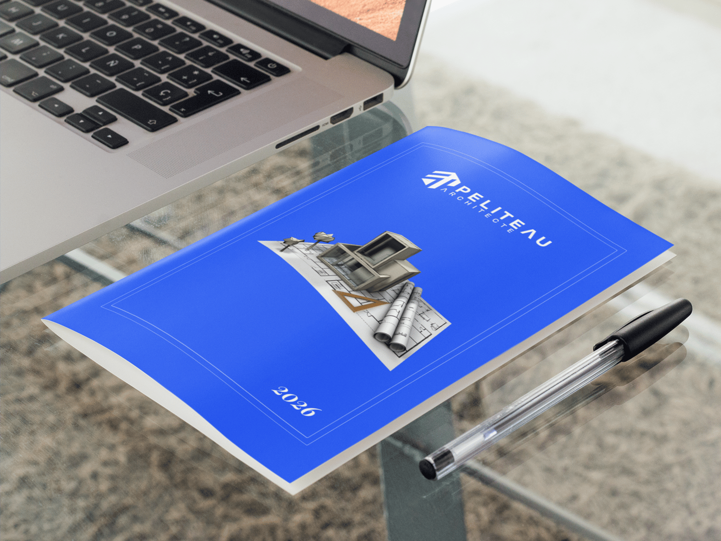 Brochure d'architecte avec plans de maison posés sur un bureau à côté d'un ordinateur portable.